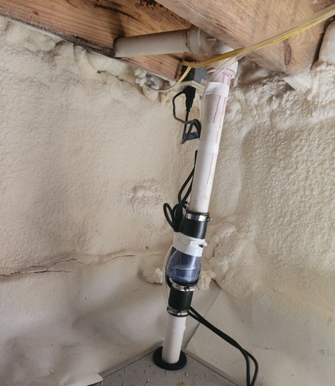 Crawl space plumbing line with backflow or check valve installed against a spray‑foam‑insulated wall.