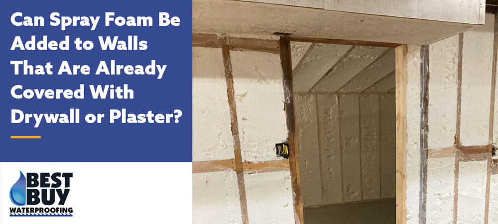 Open wall section showing spray foam insulation applied behind drywall, with exposed studs in a partially finished basement or interior wall.
